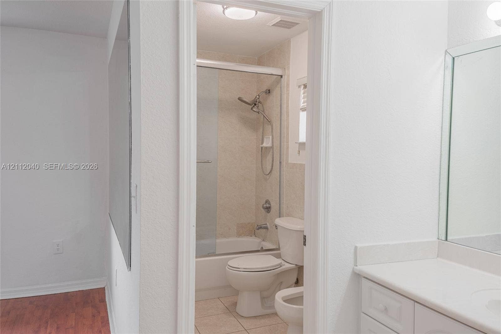 Bathroom featuring white vanity cabinetry with a solid-surface countertop, an expansive wall-mounted mirror, a tub-shower combination with a sliding glass door, and tile flooring