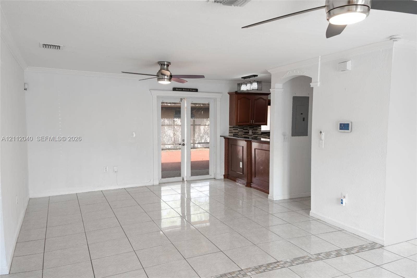 Open-concept interior featuring light-colored tile flooring, dual ceiling fans, French doors, and a kitchen peninsula with dark wood-finish cabinetry