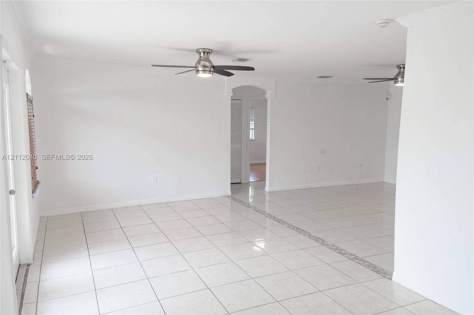 Interior space featuring polished ceramic tile flooring, dual ceiling fans with integrated lighting, and an arched doorway