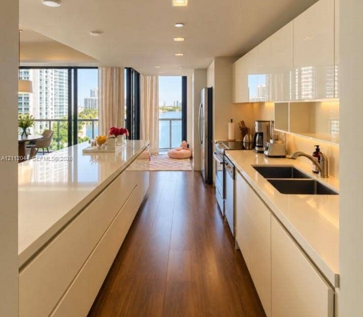 Modern kitchen featuring high-gloss cabinetry, expansive solid-surface countertops, wood-finish flooring, recessed lighting, and stainless steel appliances