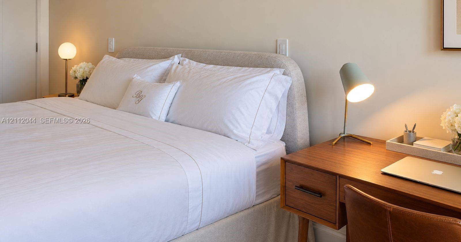 Neutral wall palette featuring a rounded upholstered headboard and wall-mounted light switches