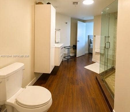 Bathroom featuring wood-finish flooring, a glass-enclosed shower, and a white wall-mounted storage cabinet