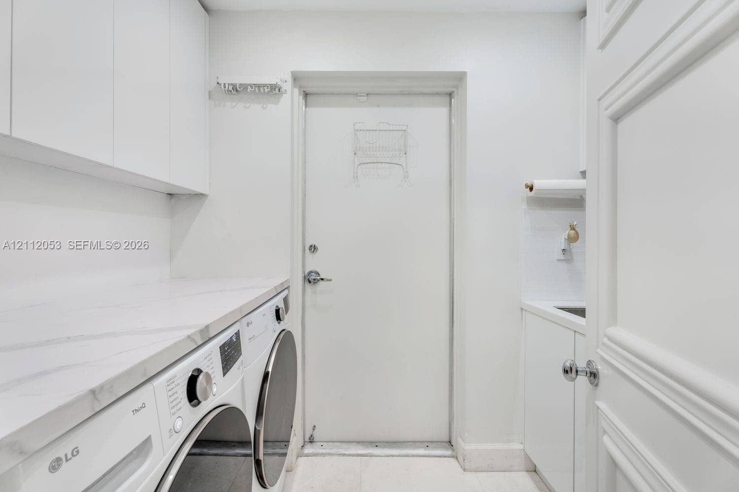 Laundry space featuring custom white cabinetry, stone-surface countertop, integrated sink, and paneled door