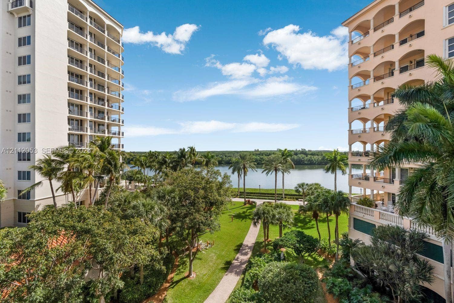 High-rise residential exterior featuring stacked arched balconies, manicured lawn, paved walkways, and palm tree landscaping