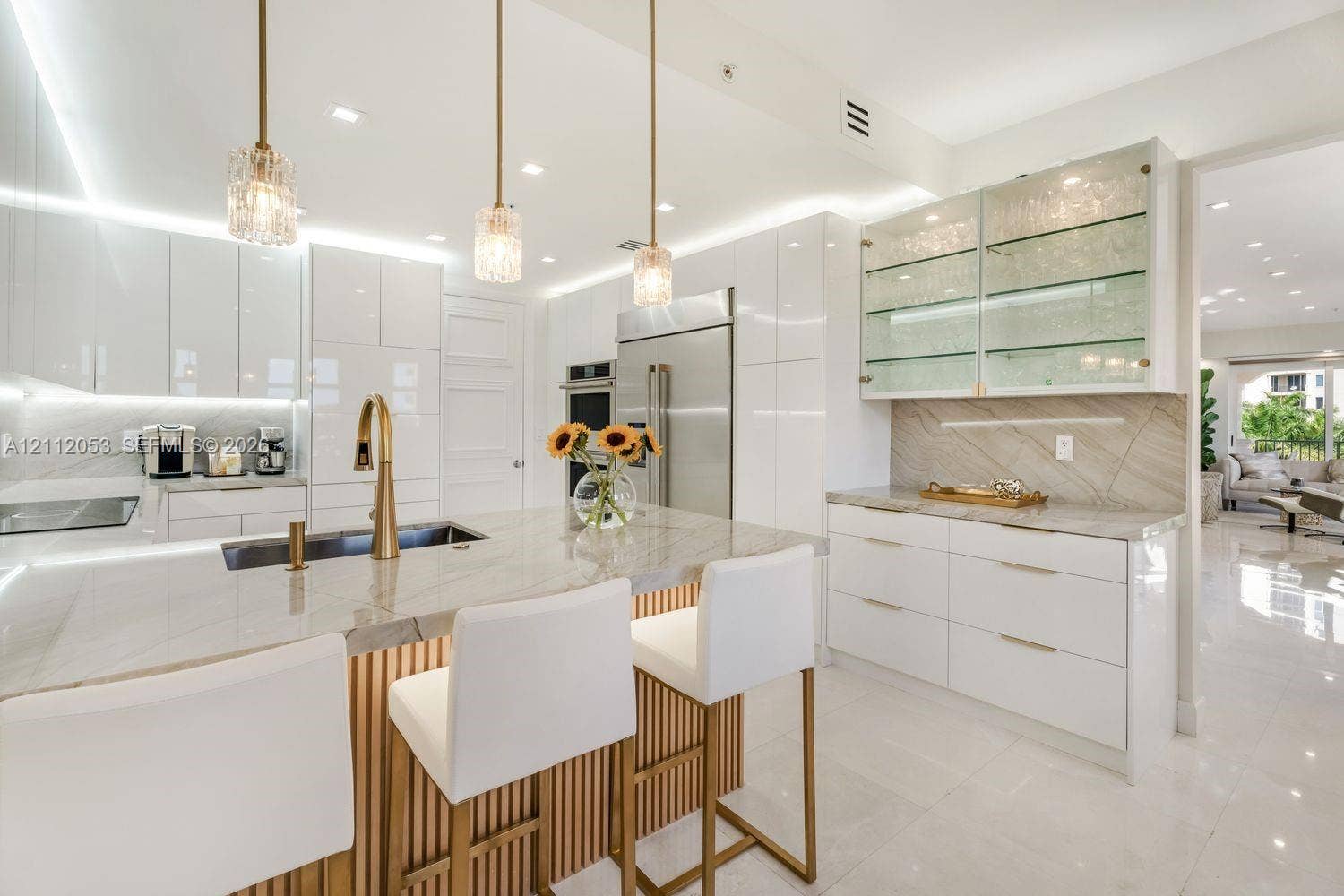 Modern kitchen featuring high-gloss cabinetry, stone-surface countertops, a center island with slat detailing, glass-front display shelving, and brass-finish hardware