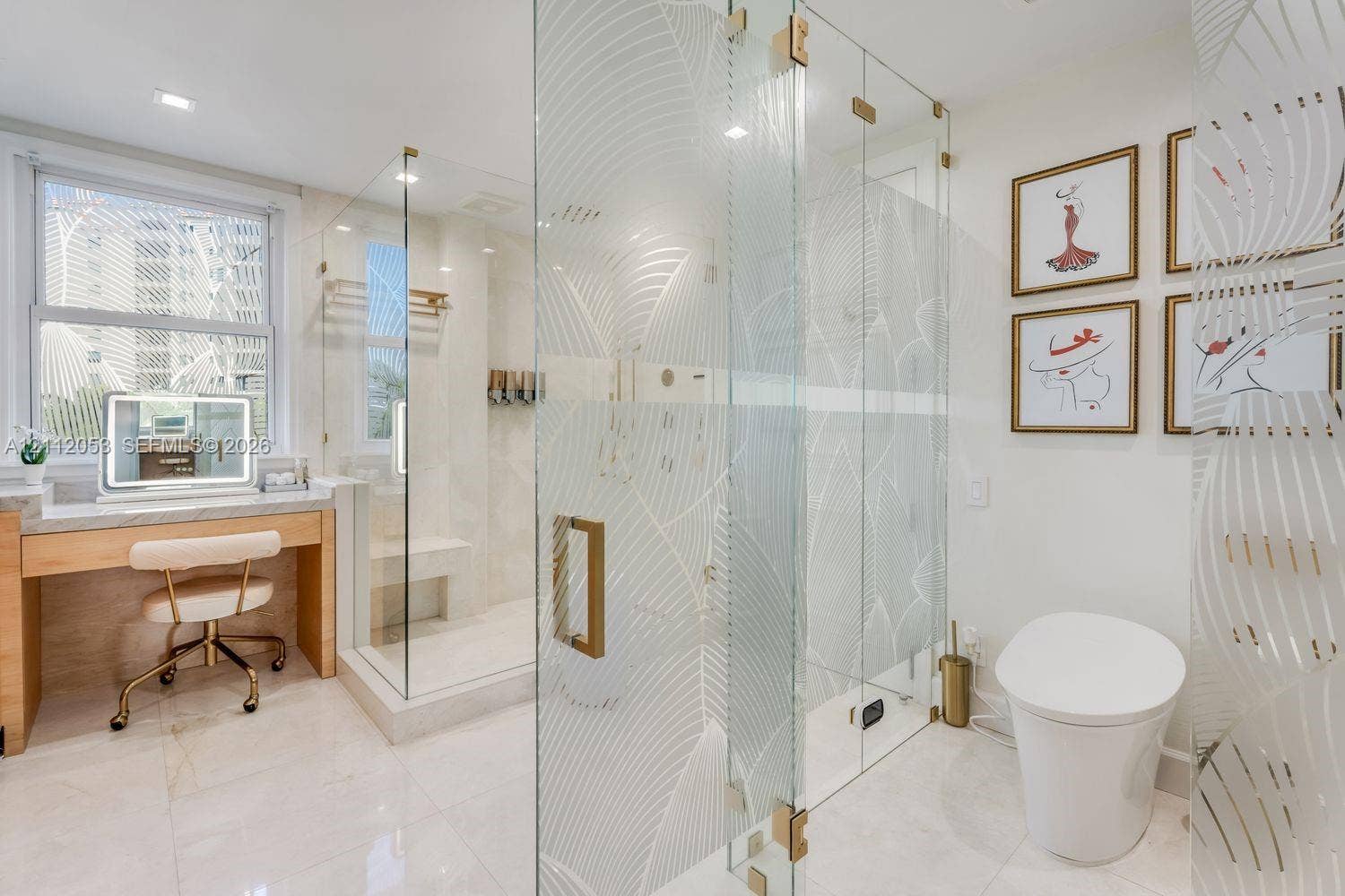 Glass-enclosed shower with etched leaf-pattern detailing, built-in stone bench, integrated vanity station with stone-finish countertop, and gold-toned hardware