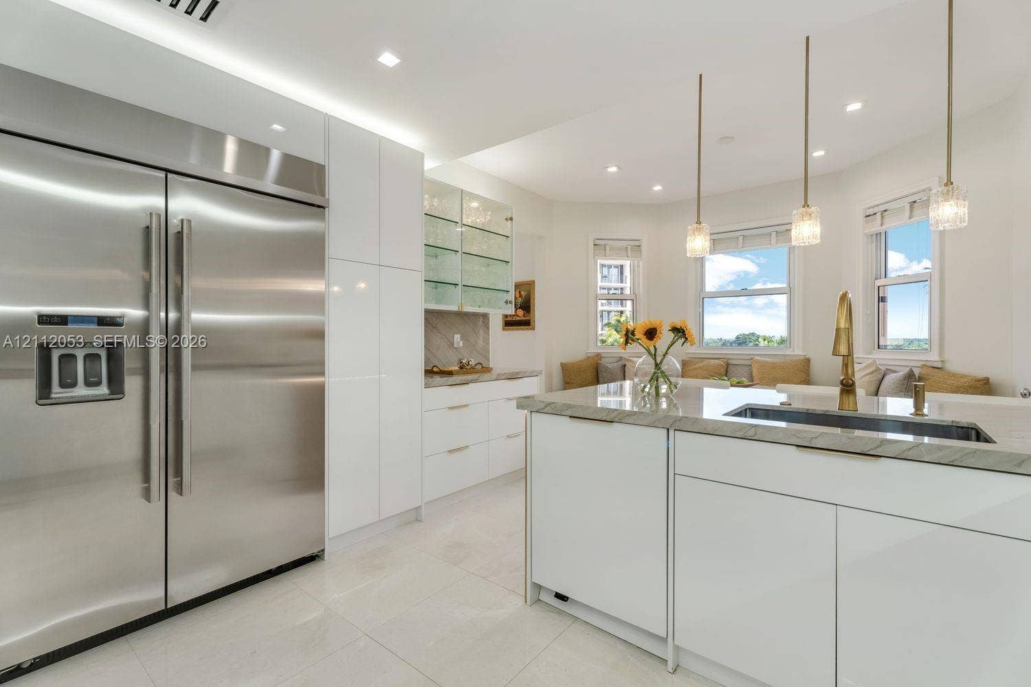 Kitchen featuring high-gloss white cabinetry, stainless steel side-by-side refrigerator, stone-topped island with a metallic faucet, and glass-front upper storage