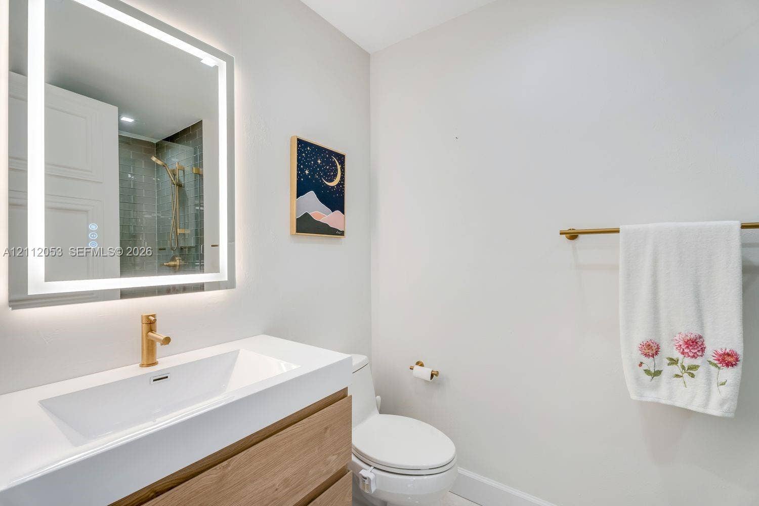 Wall-mounted illuminated mirror, wood-finish vanity with integrated sink, and brass-tone hardware