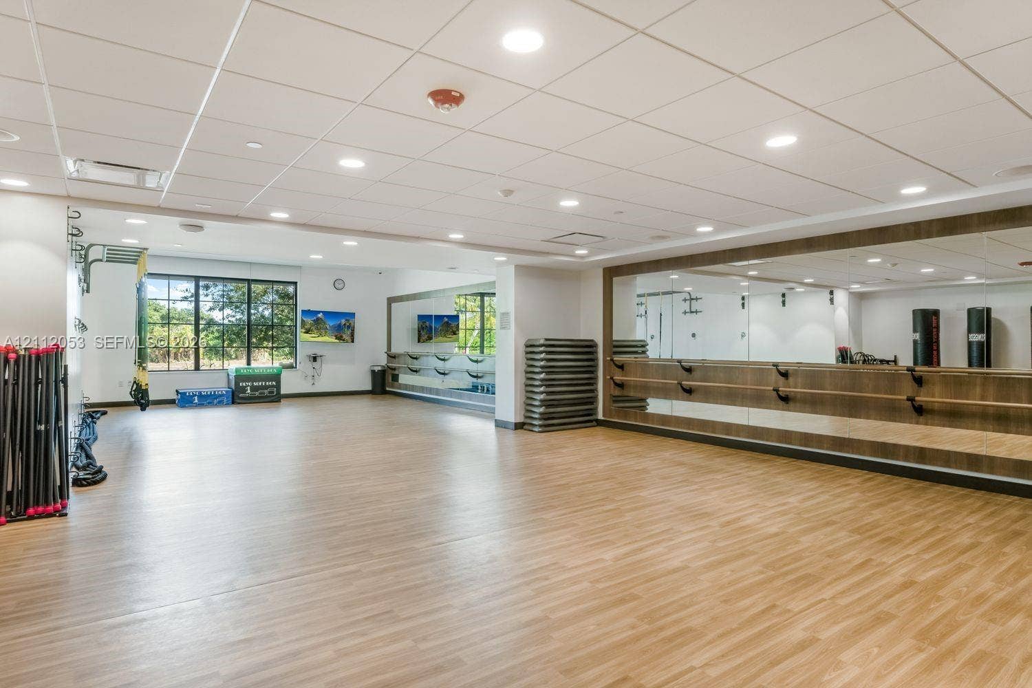 Spacious room featuring wood-finish flooring, extensive wall-mounted mirrors, recessed lighting, drop ceiling panels, and integrated horizontal wall-mounted bars