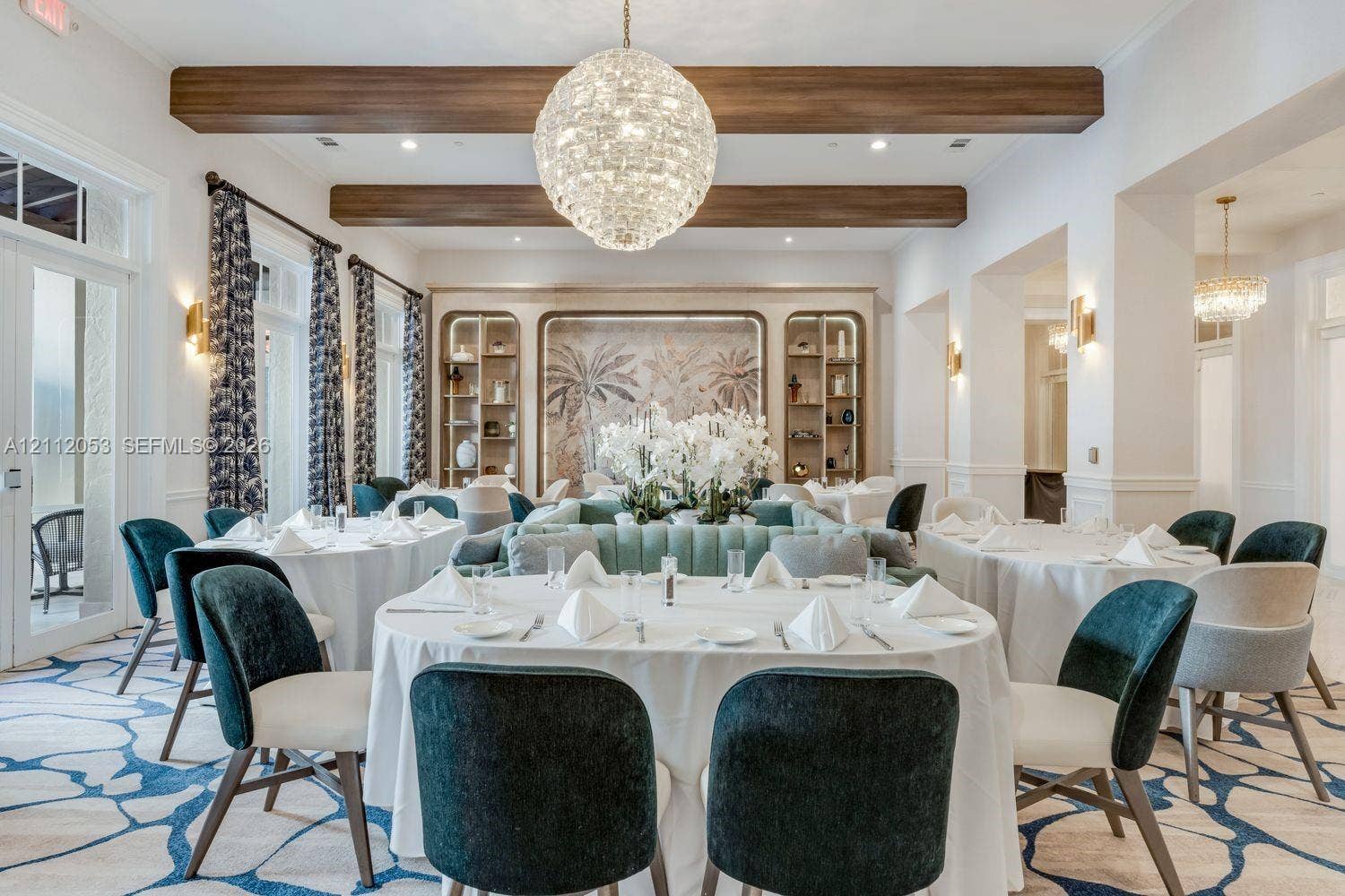 Interior space featuring exposed wood ceiling beams, a large tiered crystal chandelier, built-in recessed shelving with decorative back panels, and wall-mounted gold-toned sconces