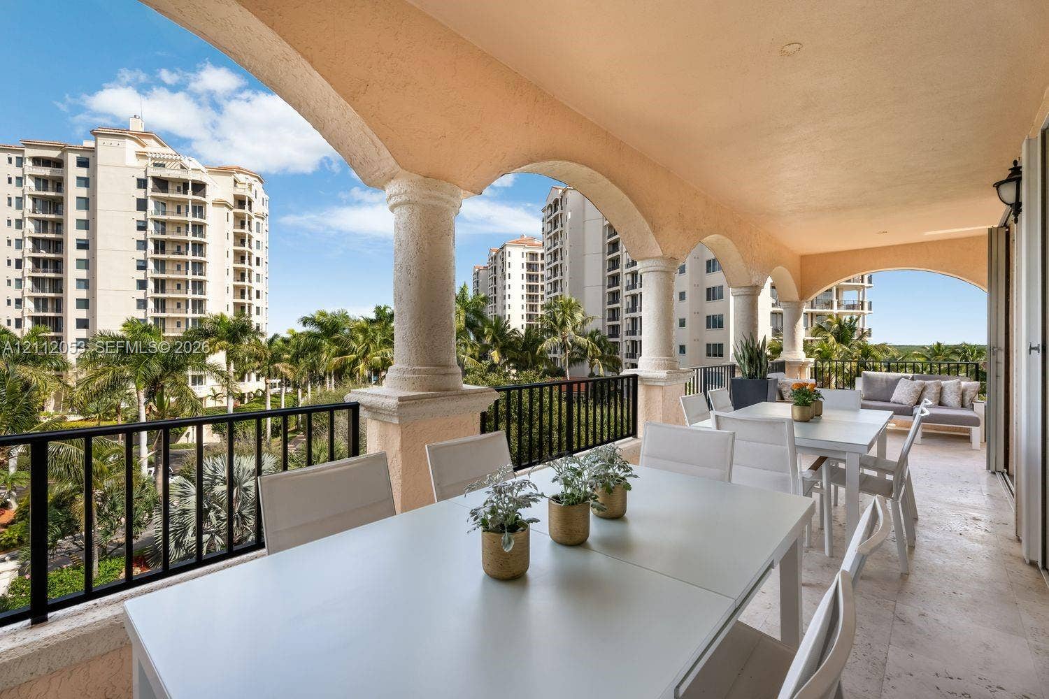 Covered balcony featuring stone-finish flooring, stucco-finished arches, textured structural columns, and black metal railings