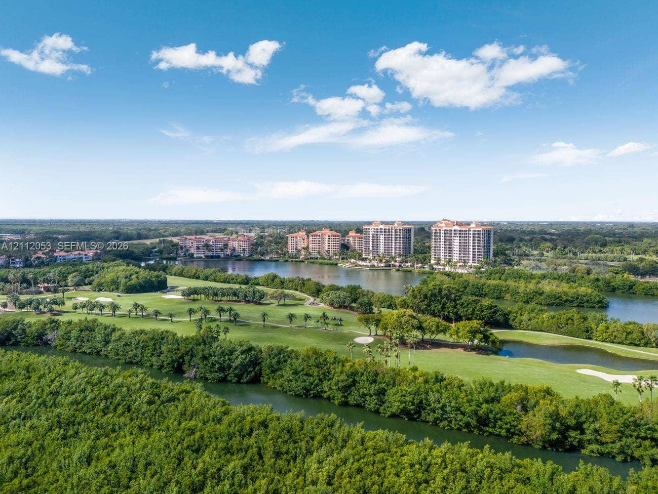 Aerial perspective featuring expansive fairways, multiple water hazards, mature vegetation, and high-rise structures