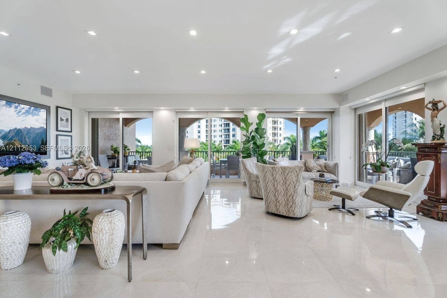 Open-concept living space featuring high-gloss tile flooring, recessed lighting, and expansive floor-to-ceiling glass sliding doors providing access to a covered balcony