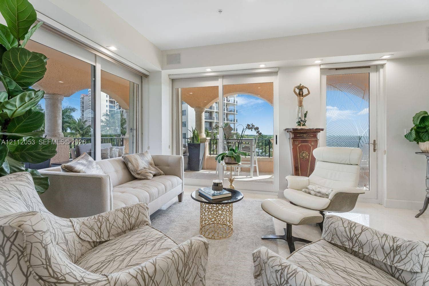 Living area featuring floor-to-ceiling glass sliding doors, recessed lighting, and polished stone flooring, opening to a covered terrace with decorative columns