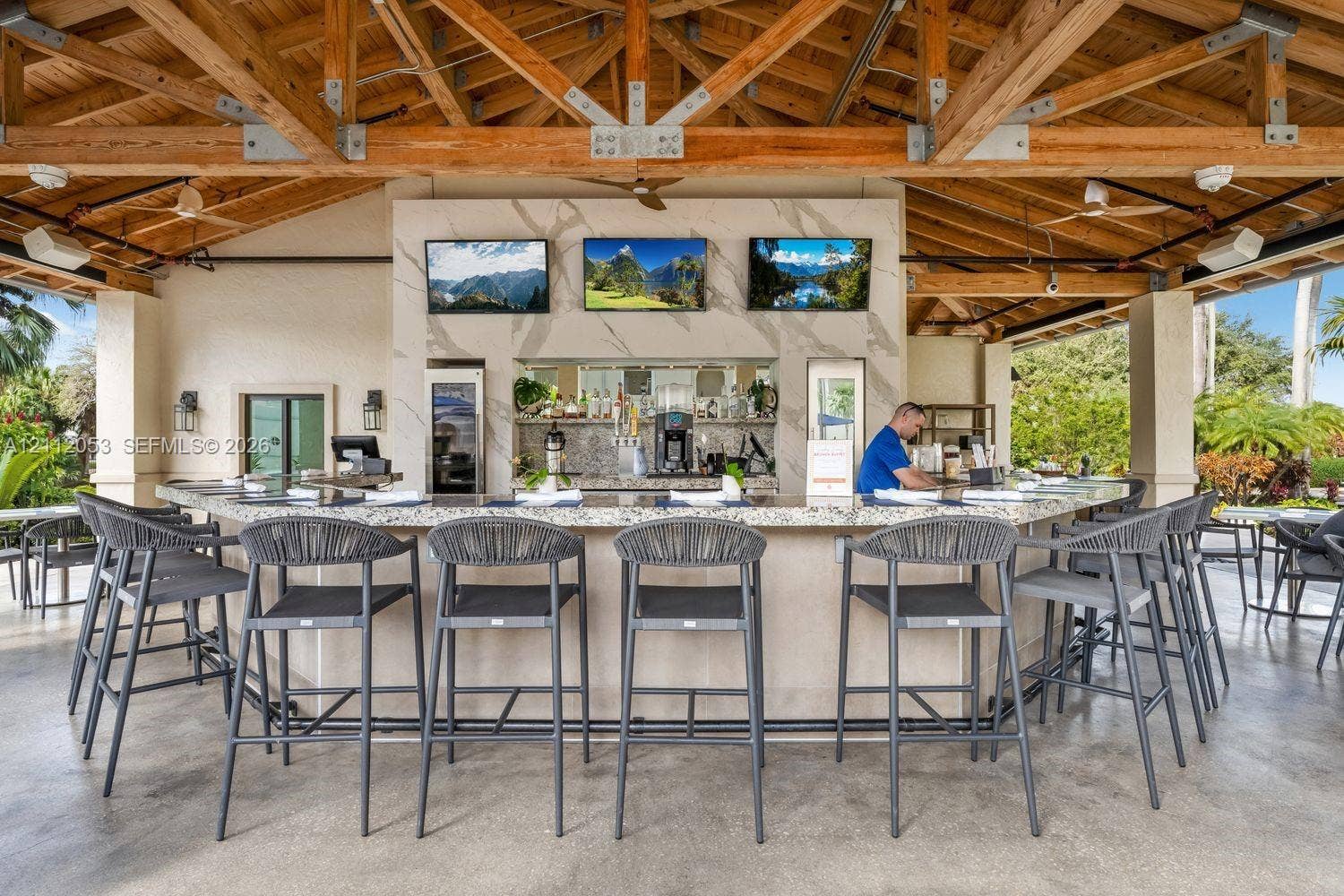 Covered outdoor bar featuring a high-contrast stone-patterned backsplash, expansive stone countertop, natural wood vaulted ceiling trusses, and recessed lighting