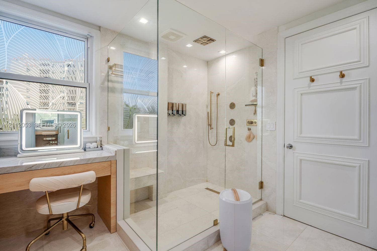Glass-enclosed walk-in shower with integrated bench seating, wall-mounted metallic fixtures, stone-finish tiling, built-in stone vanity, and multi-panel interior door