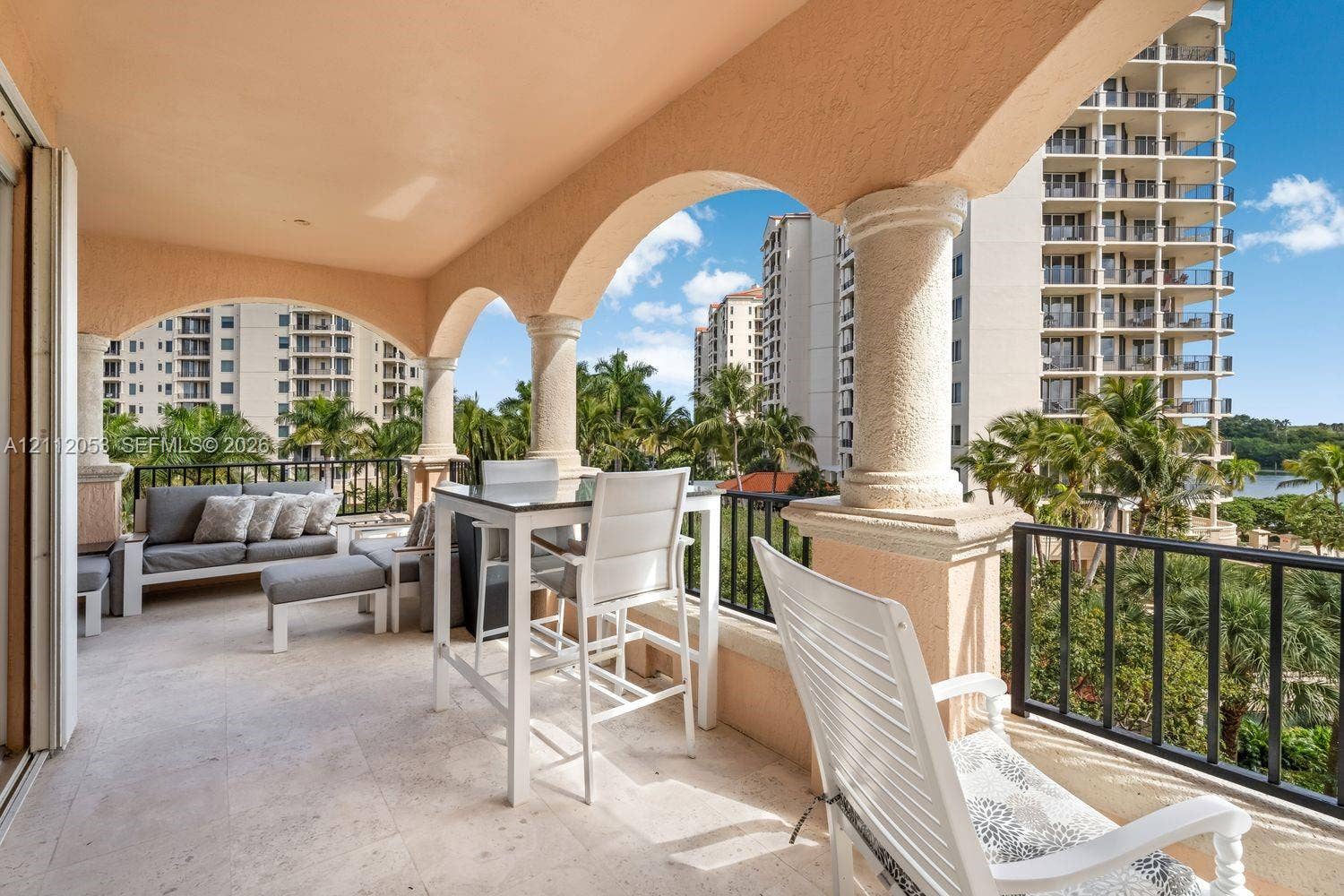 Covered balcony featuring arched stucco openings, decorative columns, stone-finish flooring, and black metal railings