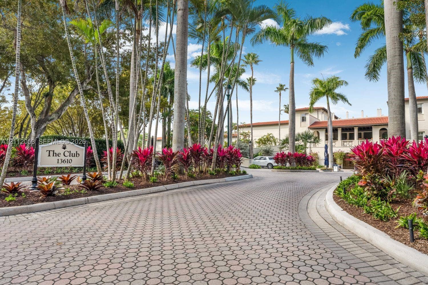 Paved stone driveway featuring mature palm trees, professional tropical landscaping, and a detailed entrance monument