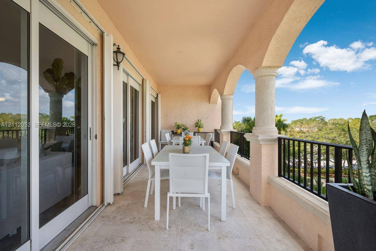 Covered balcony featuring stone tile flooring, arched structural columns, and black metal railings