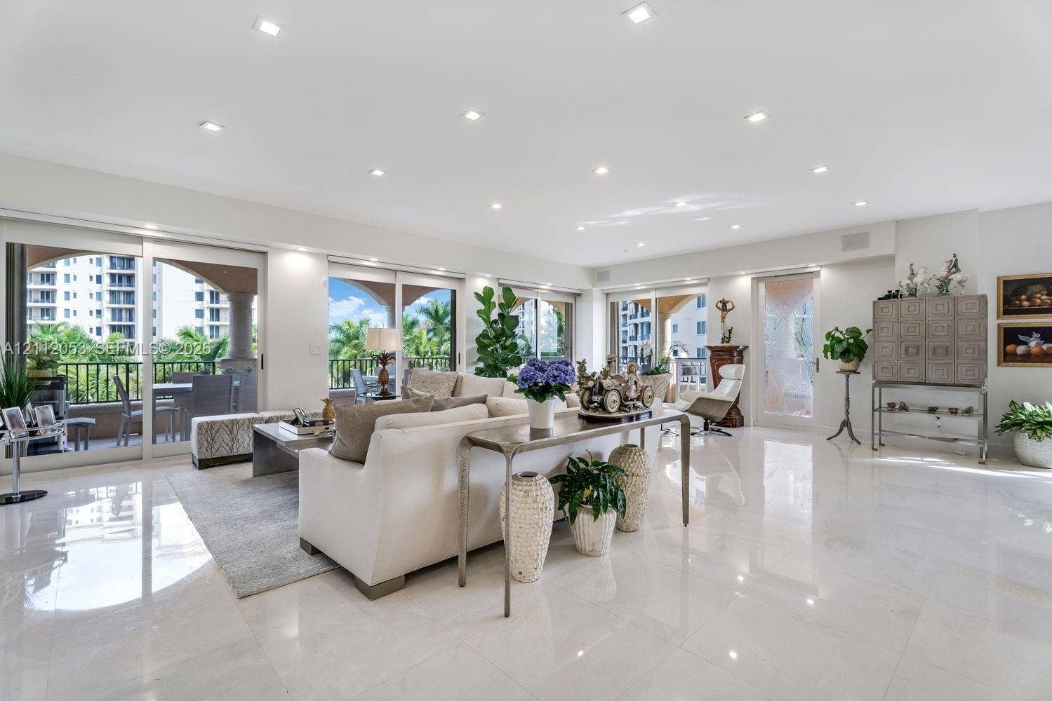 Spacious living area featuring polished stone flooring, recessed lighting, and multiple sliding glass doors providing access to a covered balcony
