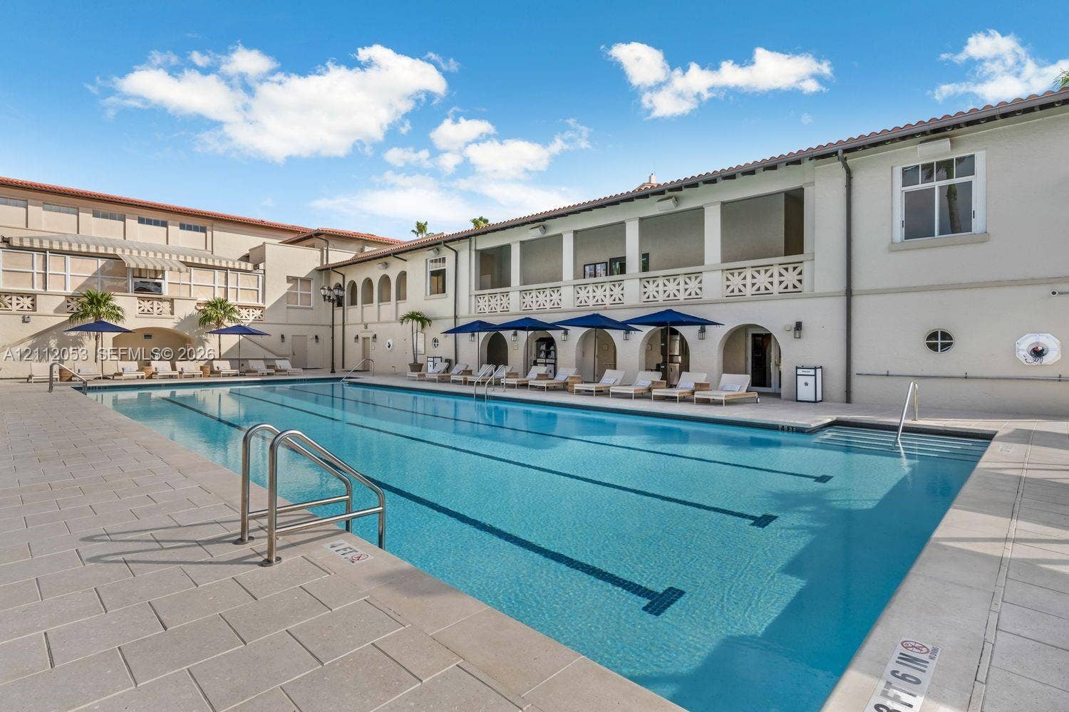 Lap pool featuring a concrete deck, multi-lane markings, metal handrails, and a covered patio area with decorative masonry accents