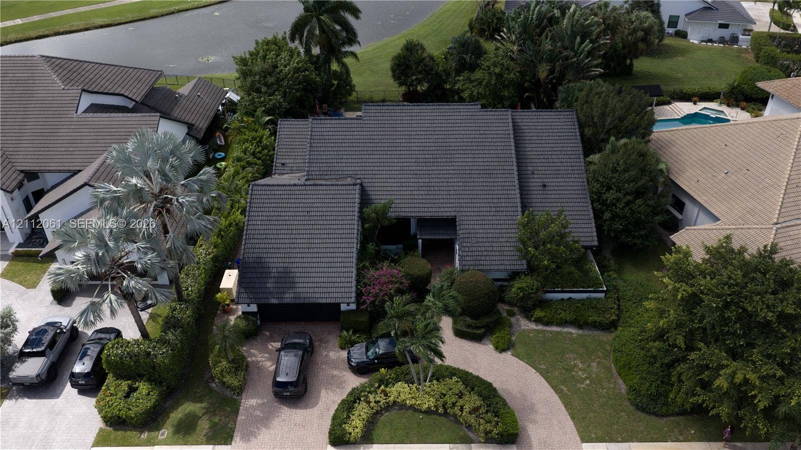 17191 SW Shaddock Lane, Boca Raton, FL 33487 Aerial perspective featuring a multi-gabled tiled roof, paver driveway, and landscaped front grounds with mature palm trees