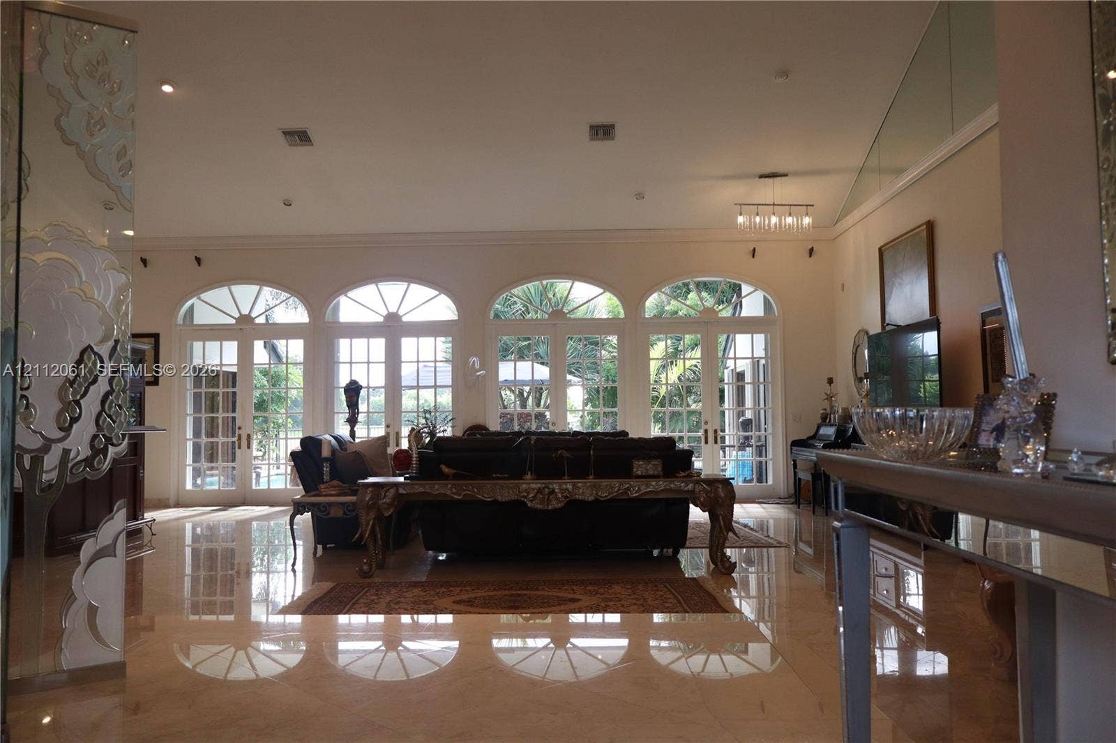 17191 SW Shaddock Lane, Boca Raton, FL 33487 Open-concept living space featuring high ceilings, polished stone flooring, four arched French doors with fanlight transoms, and a glass-paneled staircase railing