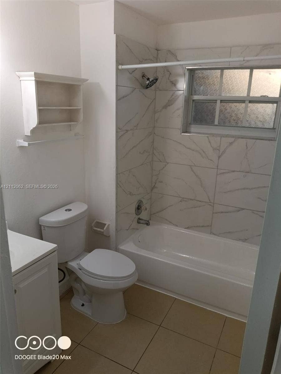 300112 NW 68th Street, #9G, Fort Lauderdale, Fort Lauderdale, FL 33309 Full bathroom featuring a tub-shower combination with large-format, stone-patterned wall tiling, light-toned ceramic floor tile, a white vanity cabinet, and a built-in wall-mounted shelving unit