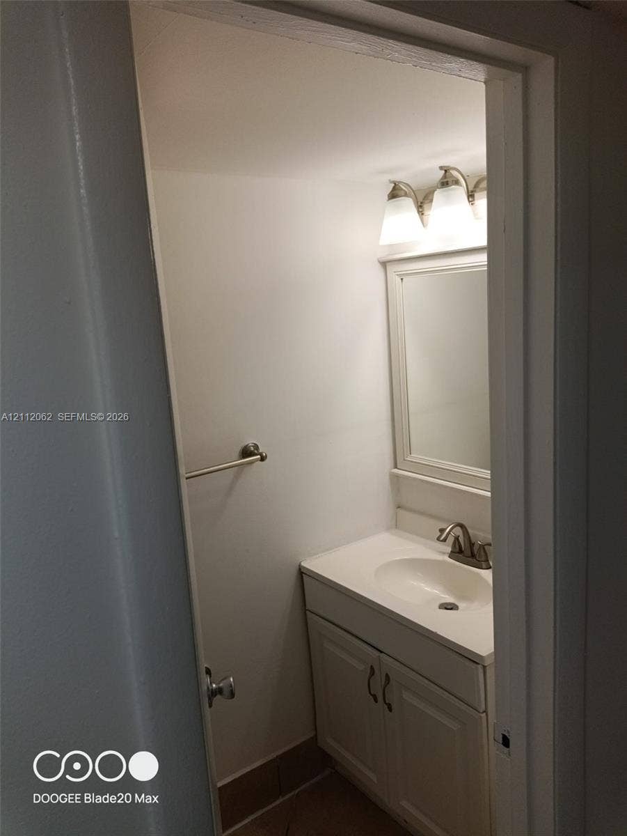 300112 NW 68th Street, #9G, Fort Lauderdale, Fort Lauderdale, FL 33309 Vanity featuring a white cabinet, solid-surface countertop with an integrated oval sink, three-light fixture with white shades, wall-mounted mirror, and brushed-finish faucet