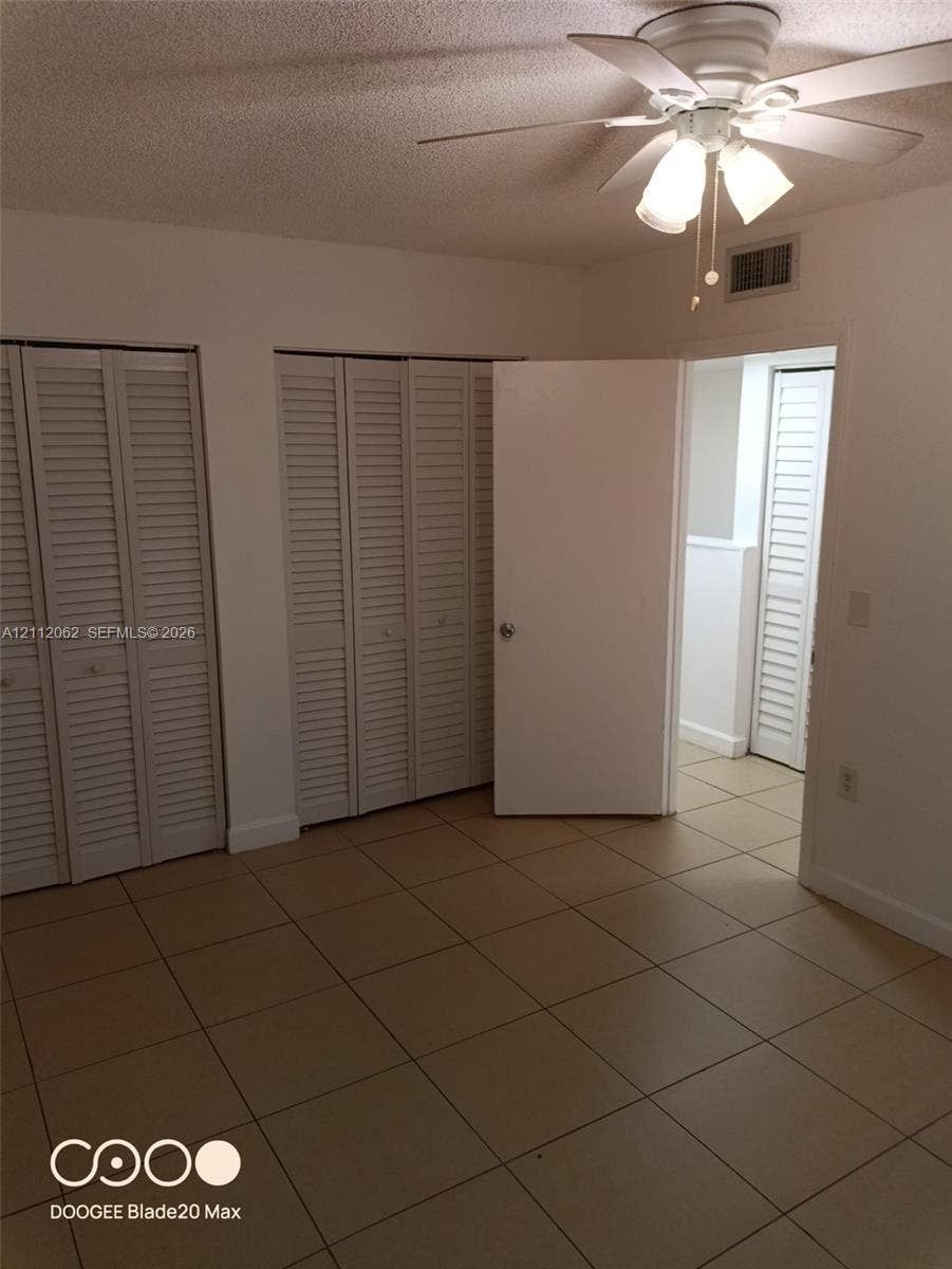 300112 NW 68th Street, #9G, Fort Lauderdale, Fort Lauderdale, FL 33309 Room featuring neutral ceramic tile flooring, dual floor-to-ceiling closets with louvered bi-fold doors, and a ceiling fan with integrated lighting