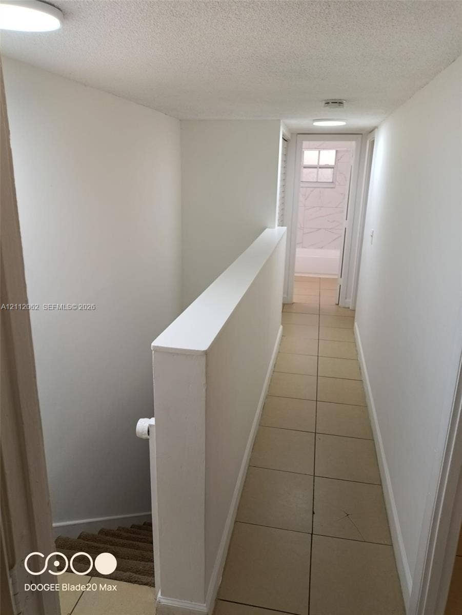 300112 NW 68th Street, #9G, Fort Lauderdale, Fort Lauderdale, FL 33309 Hallway featuring neutral large-format tile flooring, flush-mount ceiling lighting, and a painted half-wall staircase partition