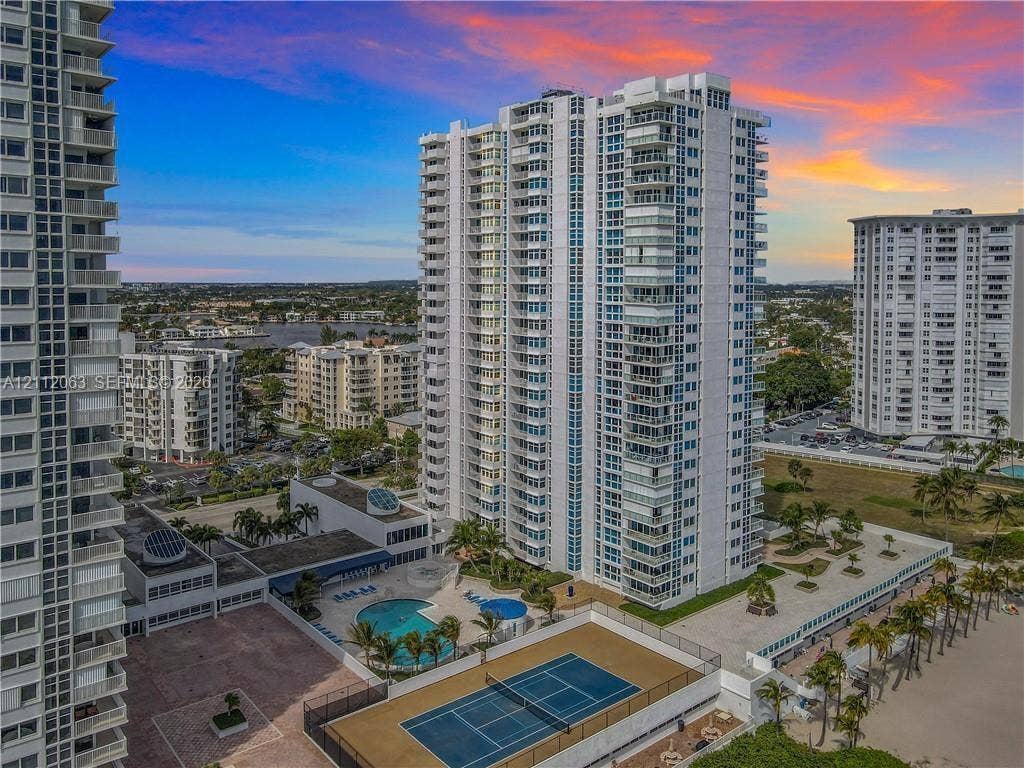 1360 S Ocean Boulevard, #2503, Pompano Beach, Pompano Beach, FL 33062 High-rise residential tower featuring private balconies, an outdoor swimming pool, a dedicated tennis court, and manicured tropical landscaping