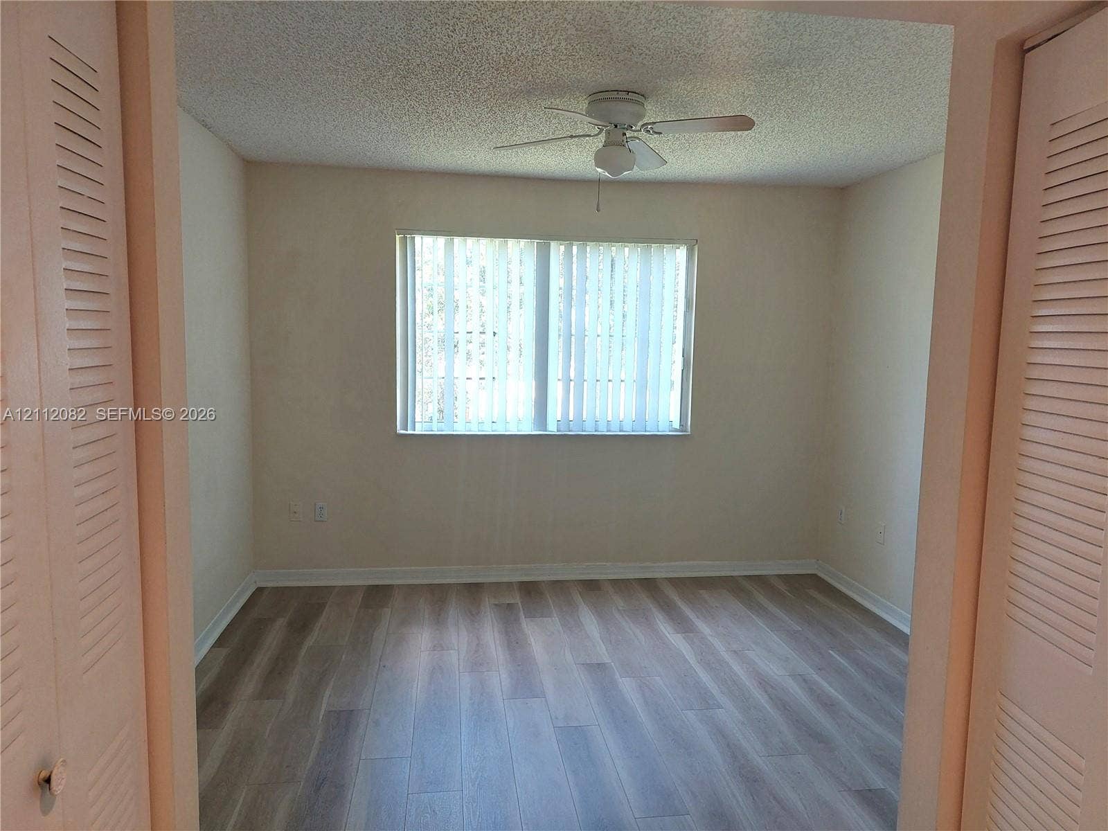 Wood-finish flooring, ceiling fan with integrated light fixture, window with vertical blinds, and dual bi-fold closet doors