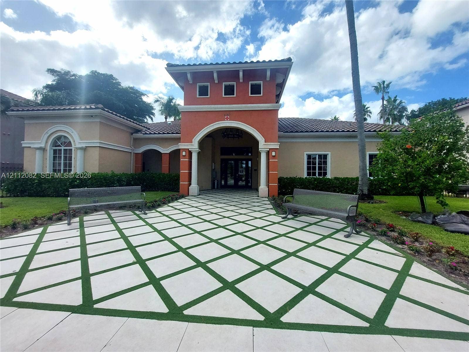 Mediterranean-inspired facade featuring an arched entryway, stucco exterior, decorative roof tiles, and a geometric-patterned paver walkway