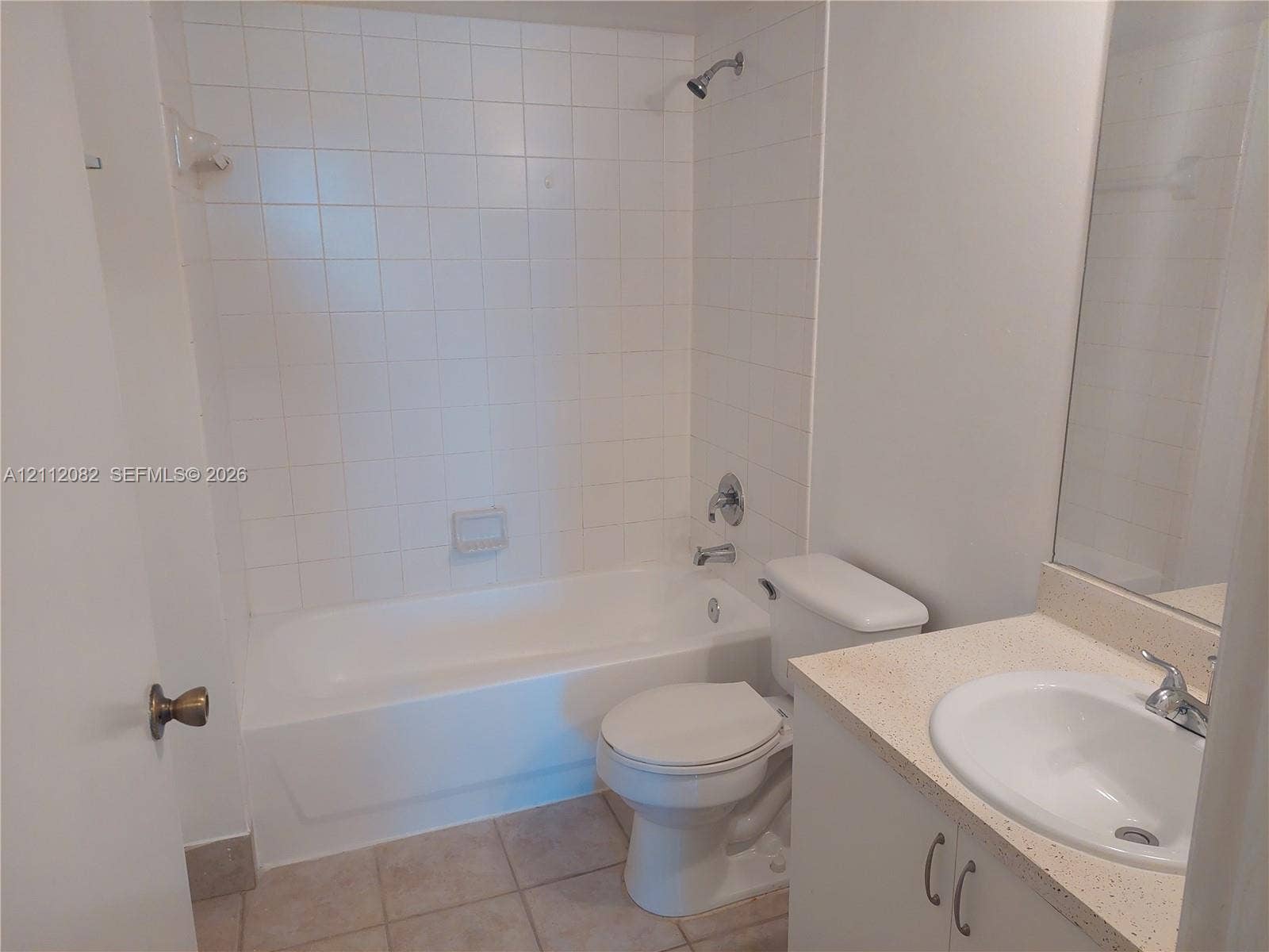 Bathroom featuring a white vanity with a solid-surface countertop, an integrated sink, floor-to-ceiling ceramic wall tile surrounding the bathtub, and neutral tile flooring