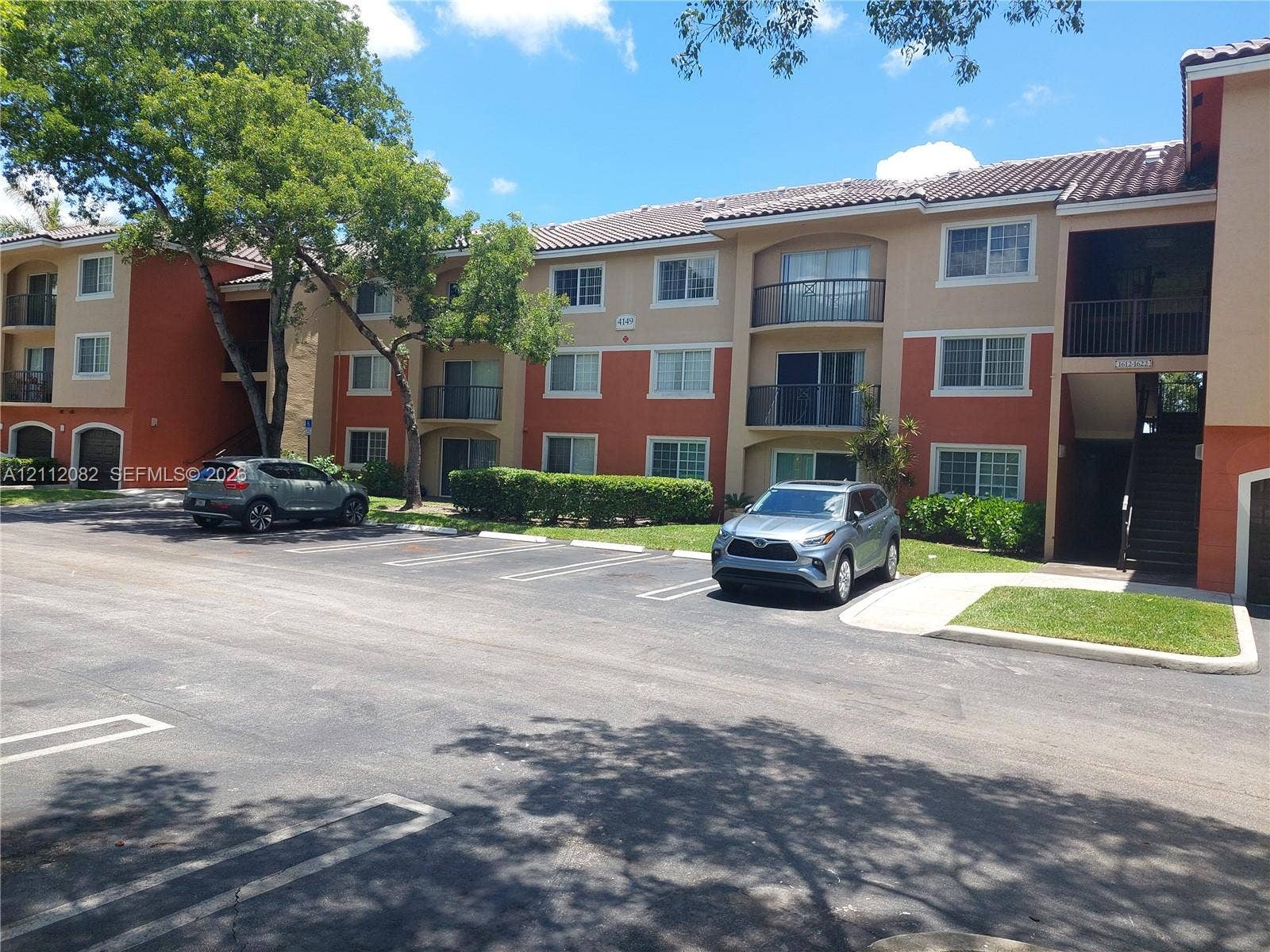Multi-story building exterior featuring a tiled roof, stucco facade, private balconies with railings, and designated surface parking