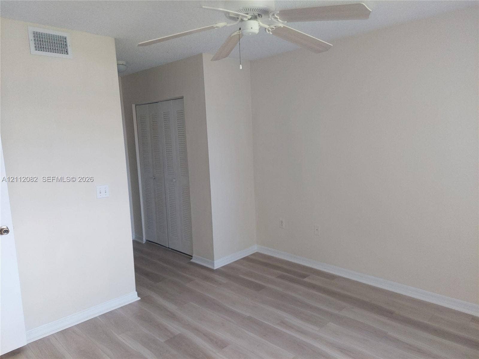 Neutral-toned interior featuring wood-finish flooring, a ceiling fan with light fixture, and louvered closet doors