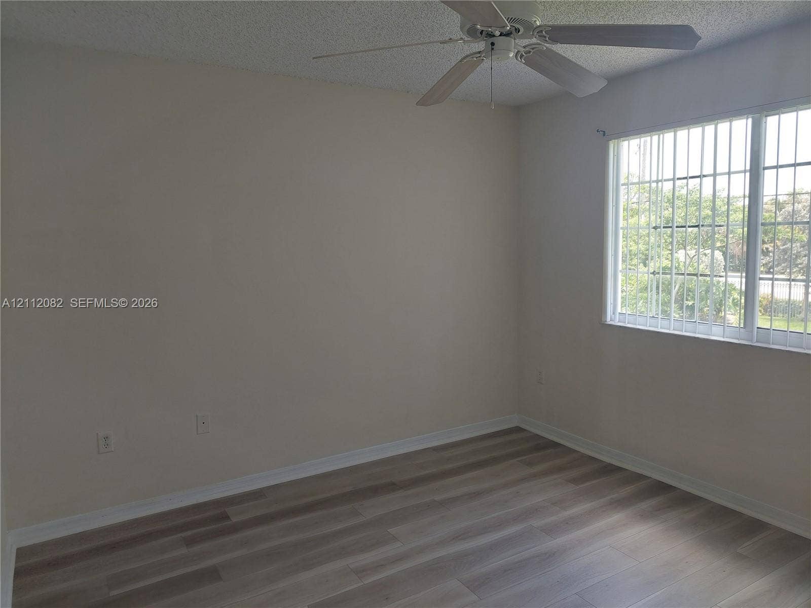 Room featuring wood-finish flooring, a multi-blade ceiling fan, and a window with security bars