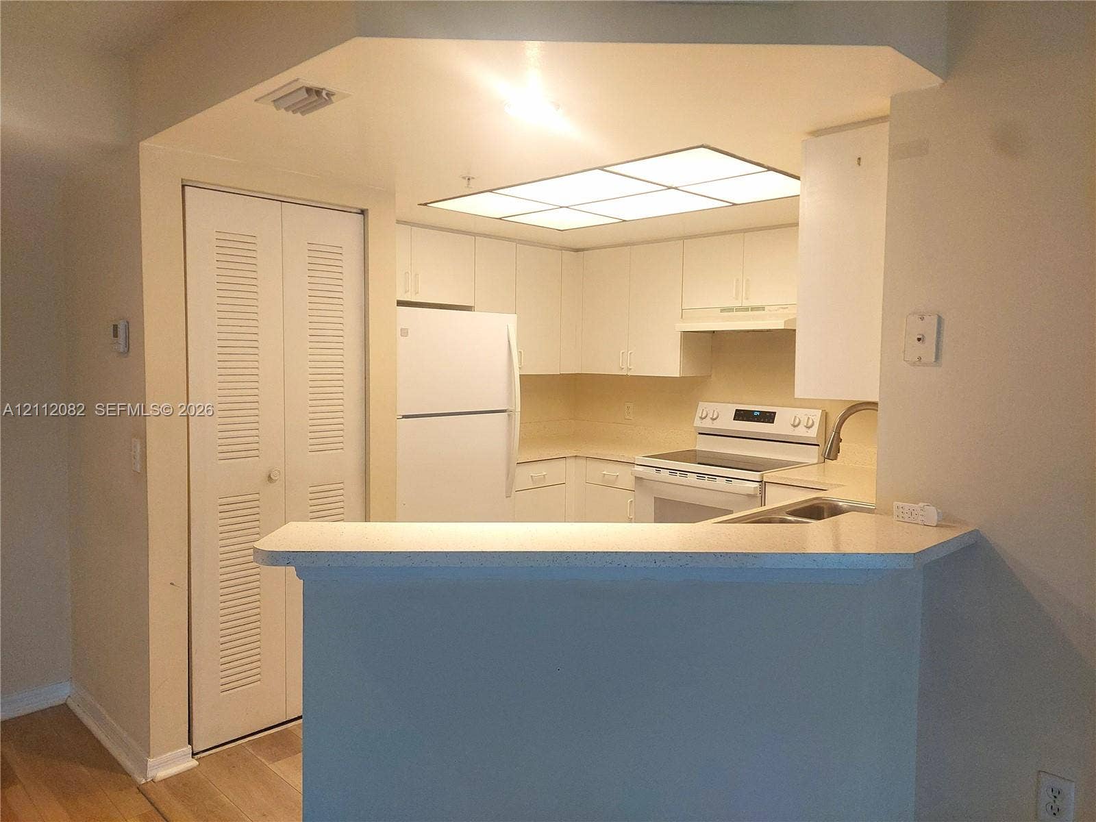 Kitchen featuring white cabinetry, solid-surface countertops, breakfast bar, recessed paneling, and integrated fluorescent lighting