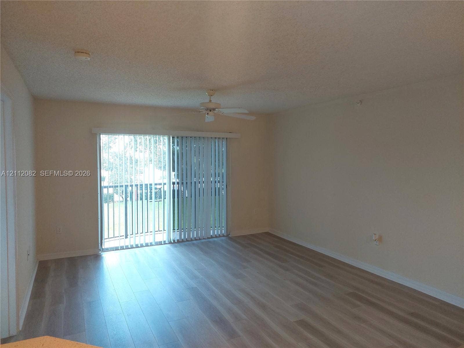 Neutral-toned interior featuring wood-finish flooring, a ceiling fan, and sliding glass doors providing access to the exterior