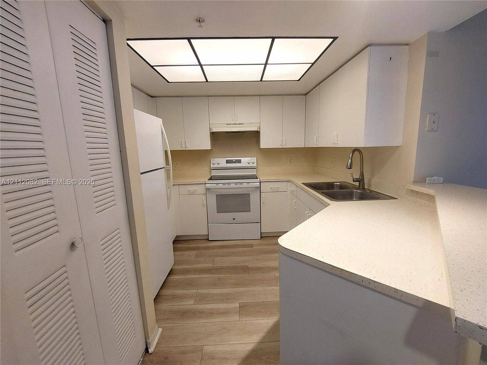 Kitchen featuring wood-finish flooring, white cabinetry, a neutral solid-surface countertop, an integrated breakfast bar, and a recessed panel light fixture