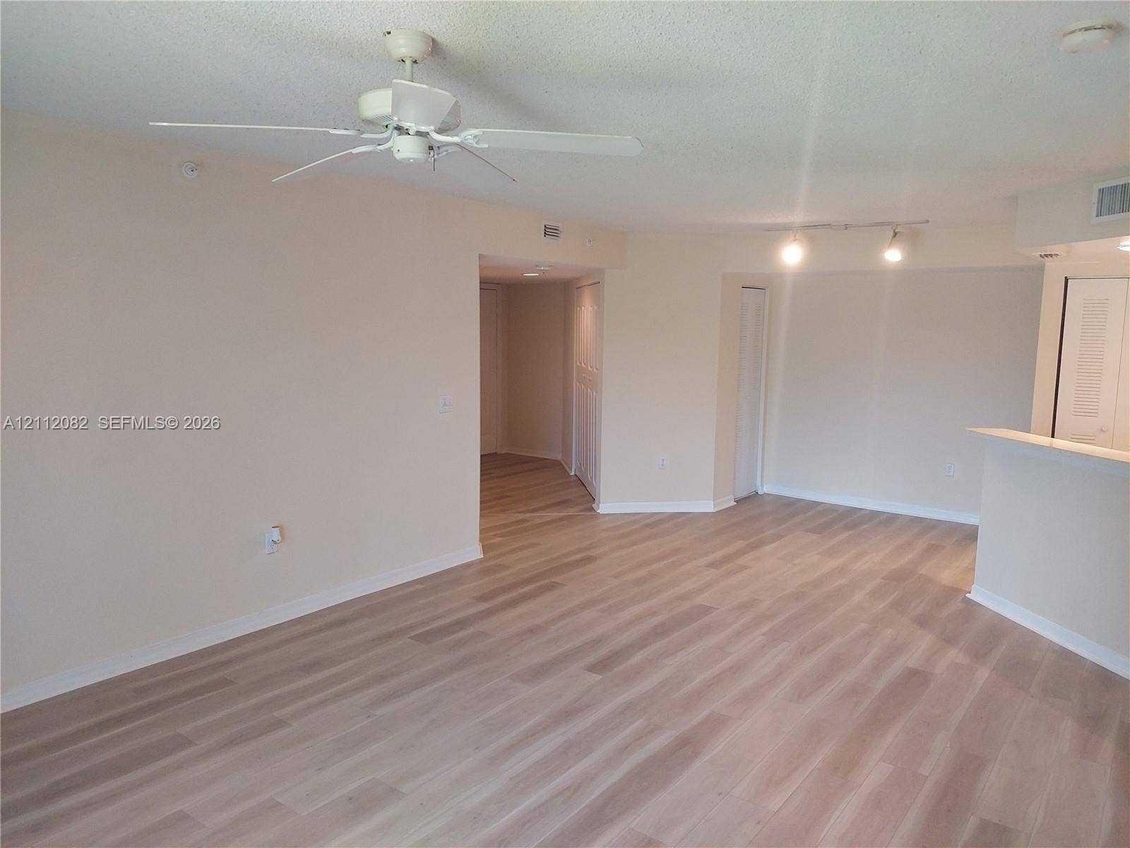 Neutral-toned living space featuring light-tone wood-finish flooring, a white ceiling fan, and adjustable track lighting