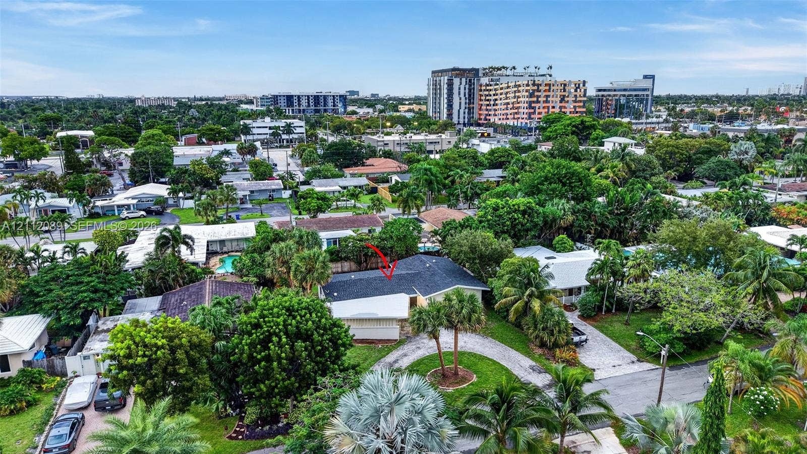 2017 NE 29th Court, Fort Lauderdale, FL 33306 Aerial perspective of a residential property featuring a dark-toned shingled roof, a curved driveway, and established palm trees within a landscaped lot