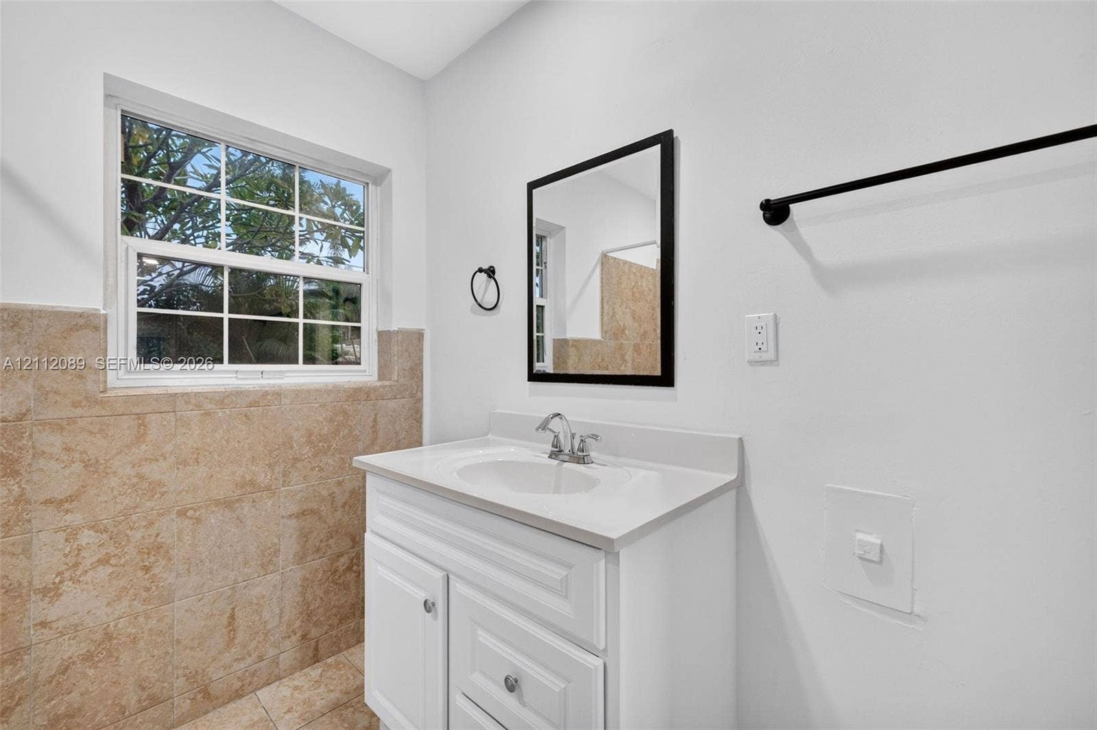 2017 NE 29th Court, Fort Lauderdale, FL 33306 Single-sink vanity with a solid-surface countertop, neutral tile wainscoting, framed wall mirror, and matte black hardware