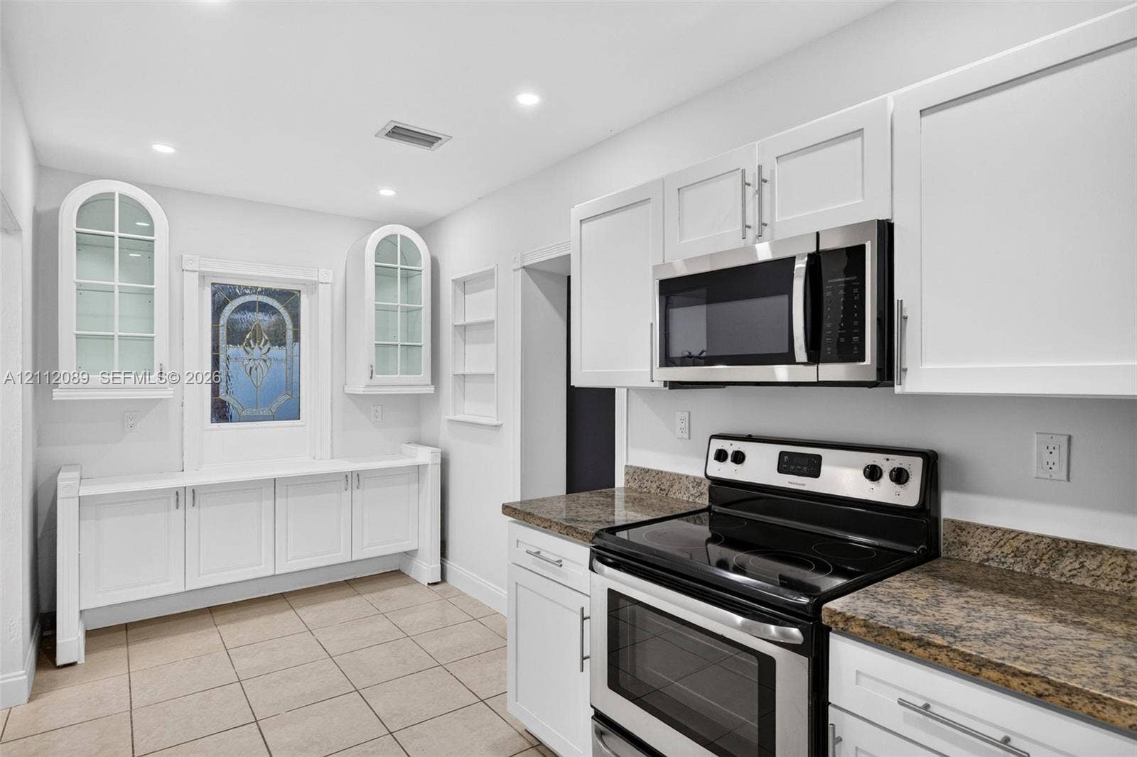 2017 NE 29th Court, Fort Lauderdale, FL 33306 White Shaker-style cabinetry, stone-finish countertops, stainless steel appliances, arched glass-panel wall cabinetry, and tile flooring