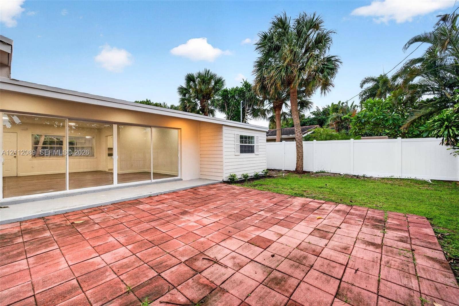 2017 NE 29th Court, Fort Lauderdale, FL 33306 Backyard featuring a red paver patio, white vinyl privacy fencing, and mature palm trees