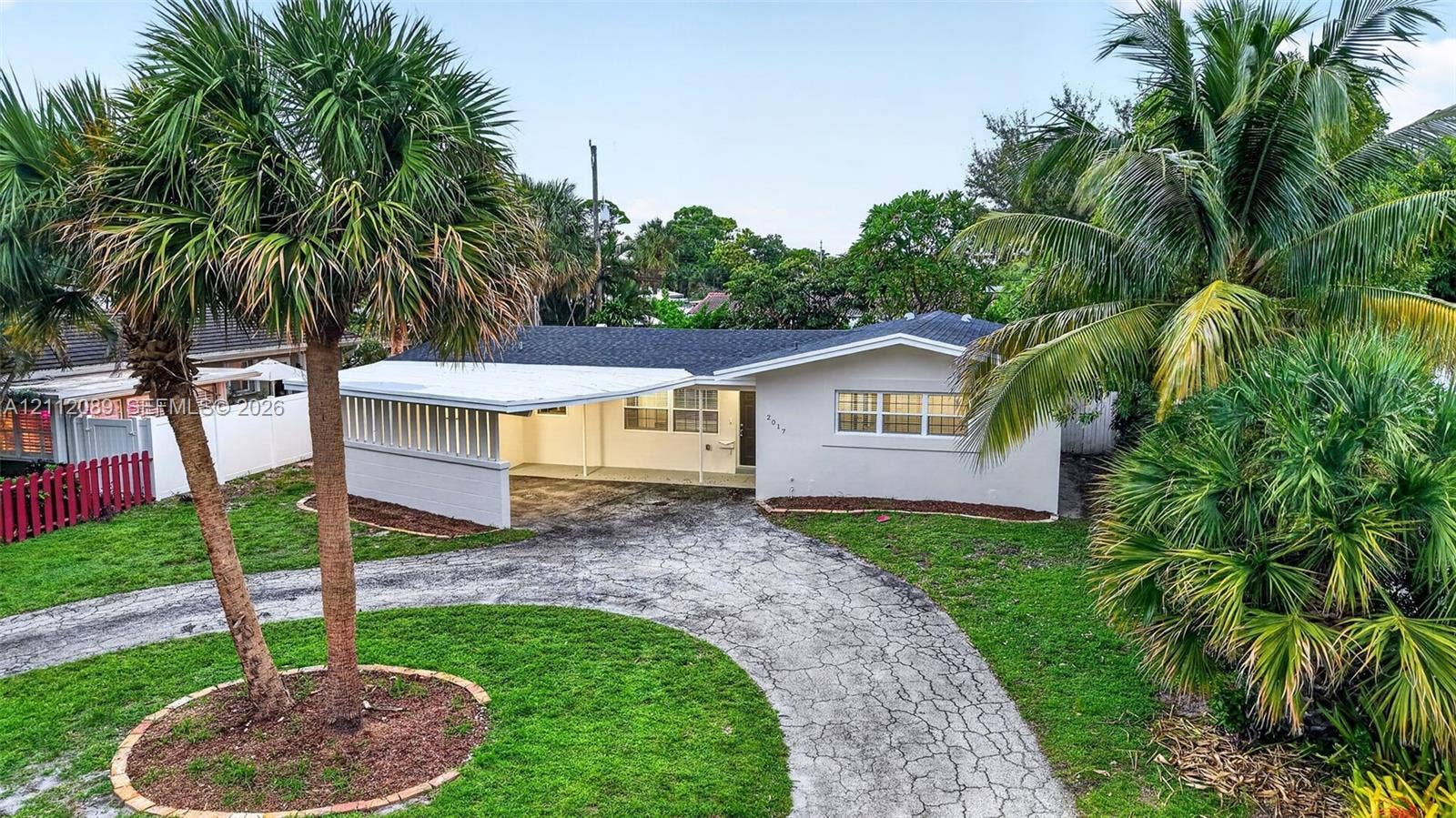 2017 NE 29th Court, Fort Lauderdale, FL 33306 Single-story residence featuring a covered carport, crisp white exterior finish, multi-pane windows, and mature palm landscaping situated on a manicured lawn