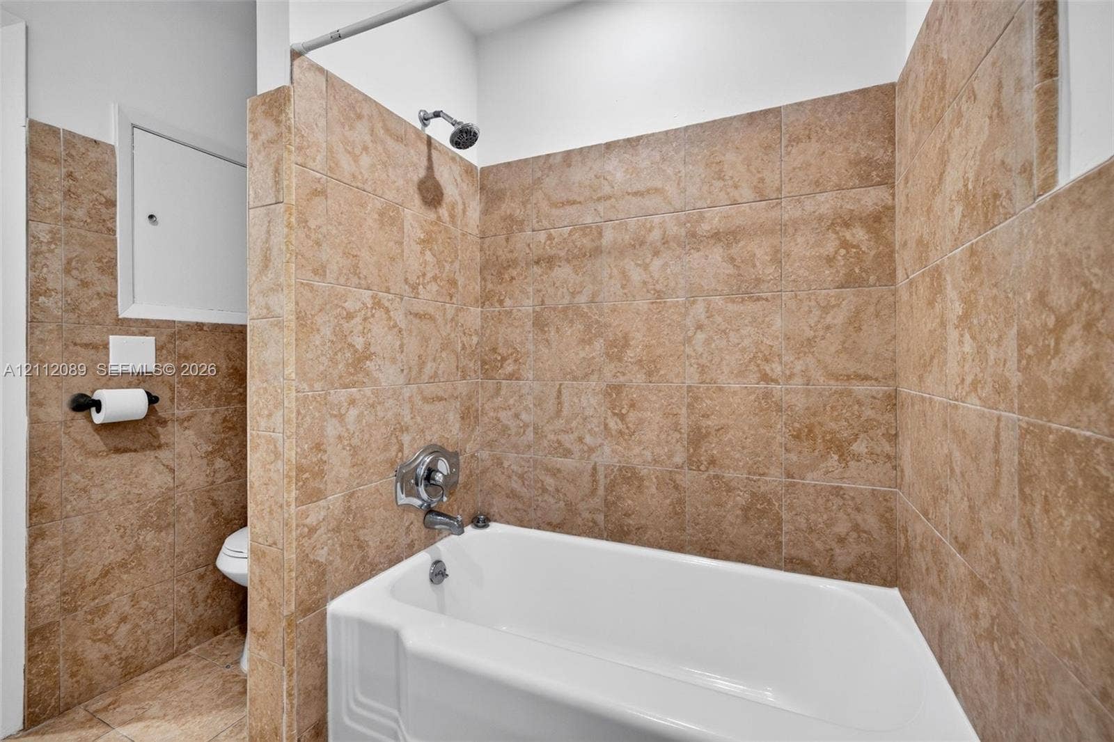 2017 NE 29th Court, Fort Lauderdale, FL 33306 Full-height tan stone-finish tile surround, white acrylic soaking tub, wall-mounted showerhead, and integrated chrome faucet hardware