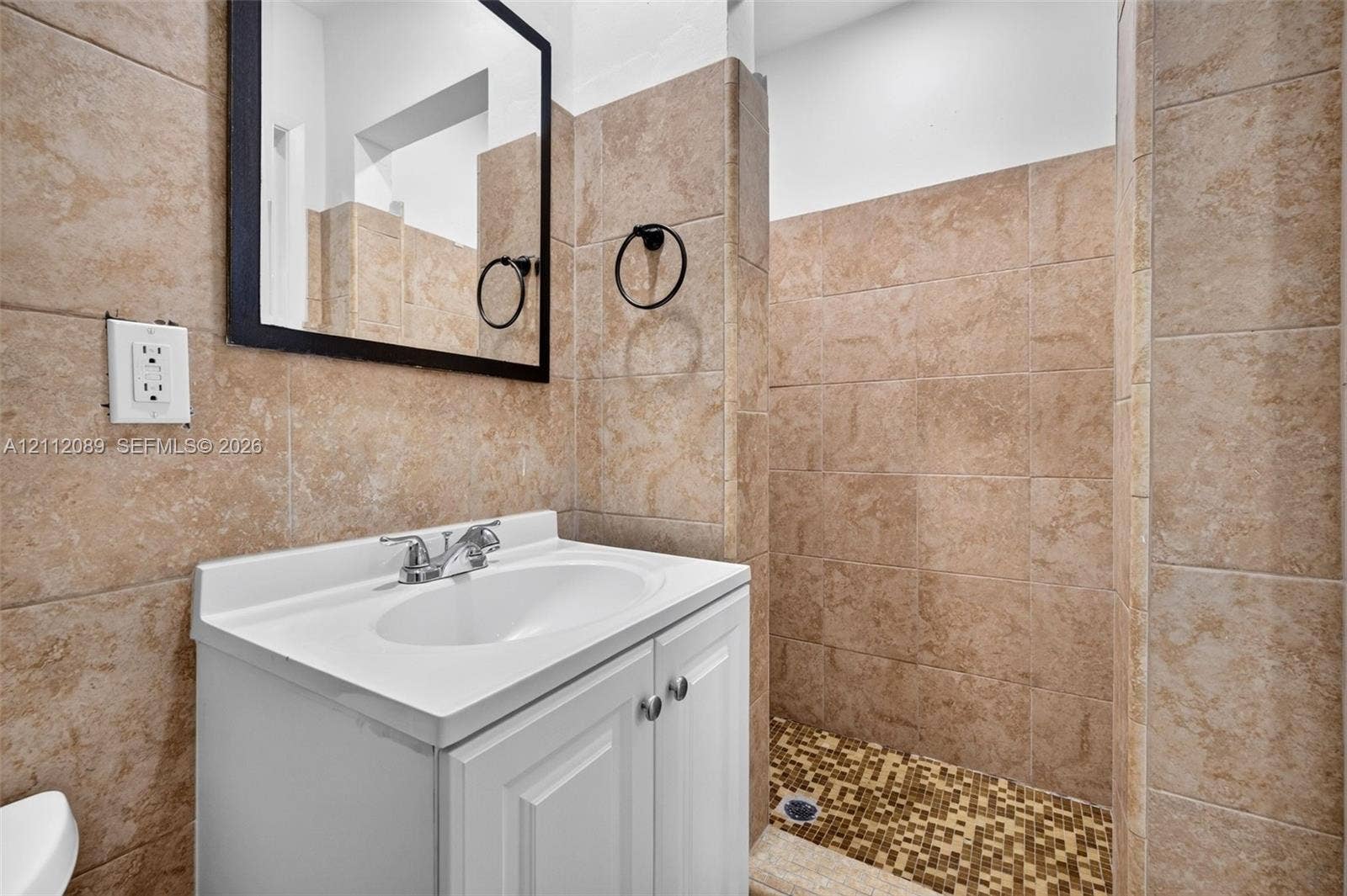 2017 NE 29th Court, Fort Lauderdale, FL 33306 White vanity with integrated basin, chrome-finish dual-handle faucet, wall-mounted black-framed mirror, and full-height stone-finish tile surround with a mosaic tile shower floor