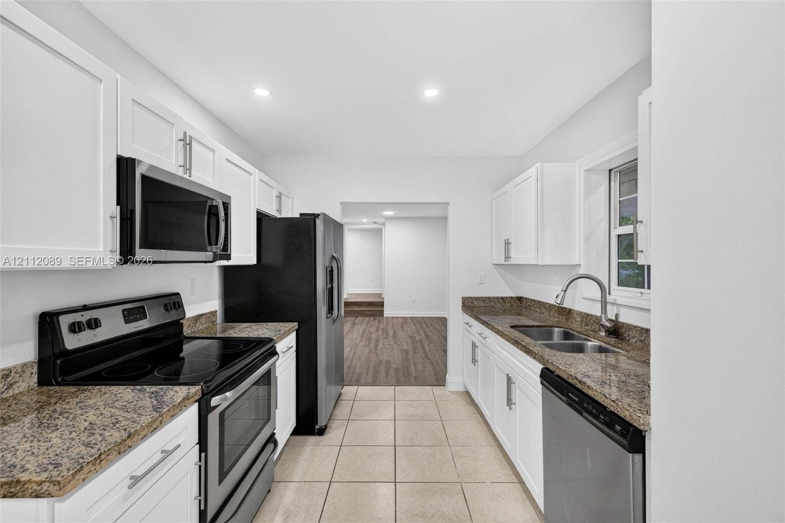 2017 NE 29th Court, Fort Lauderdale, FL 33306 Kitchen featuring white Shaker-style cabinetry, stone countertops, dual-basin stainless steel sink, and stainless steel appliances including a microwave, range, and dishwasher